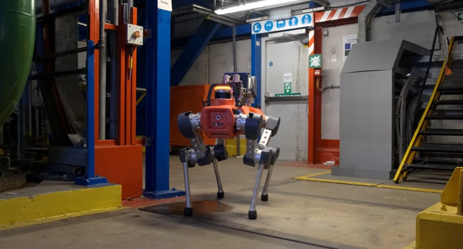 An orange four-legged ANYmal inspection robot walking across a plant floor toward a closed steel door